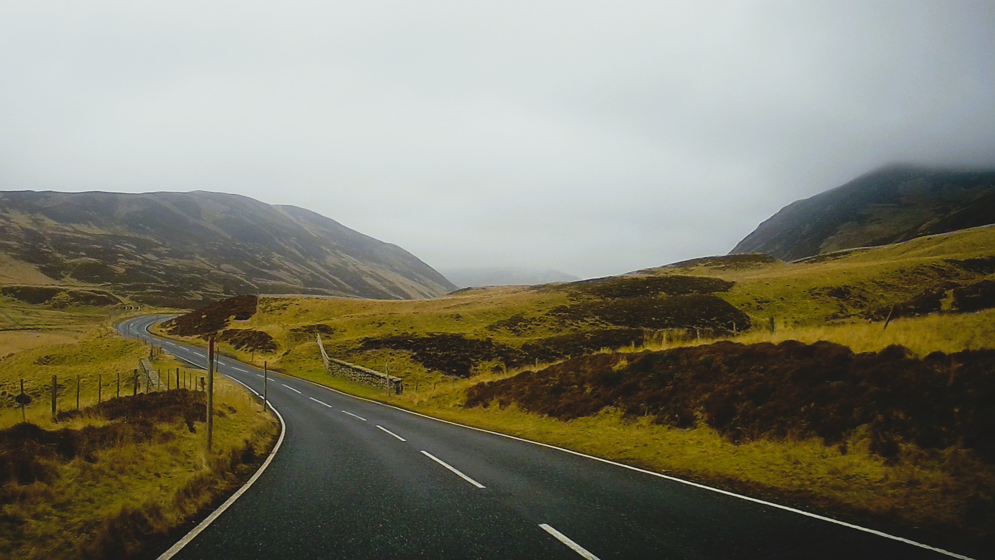 Strada che attraversa una valle delle Highlands scozzesi sotto un cielo coperto e una luce diffusa.